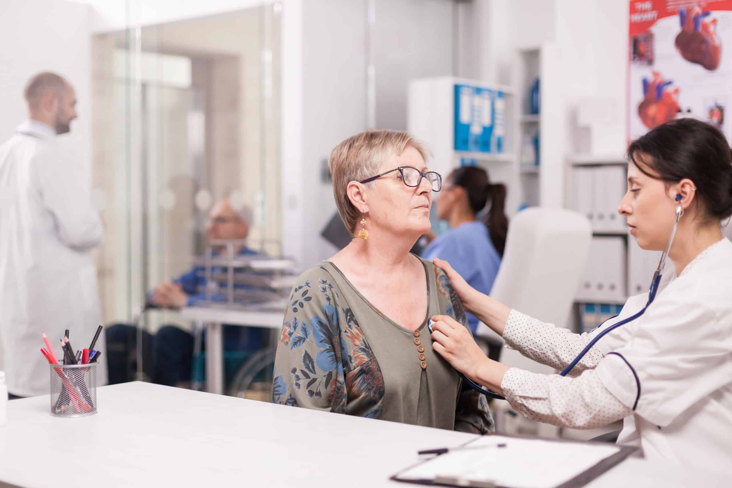 Healthcare professional examining an elderly woman in a medical clinic setting.